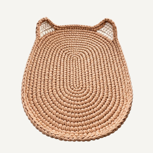 A round woven mat with cat-ear details on top, crafted from natural tan raffia or seagrass, shown on a light off-white background.