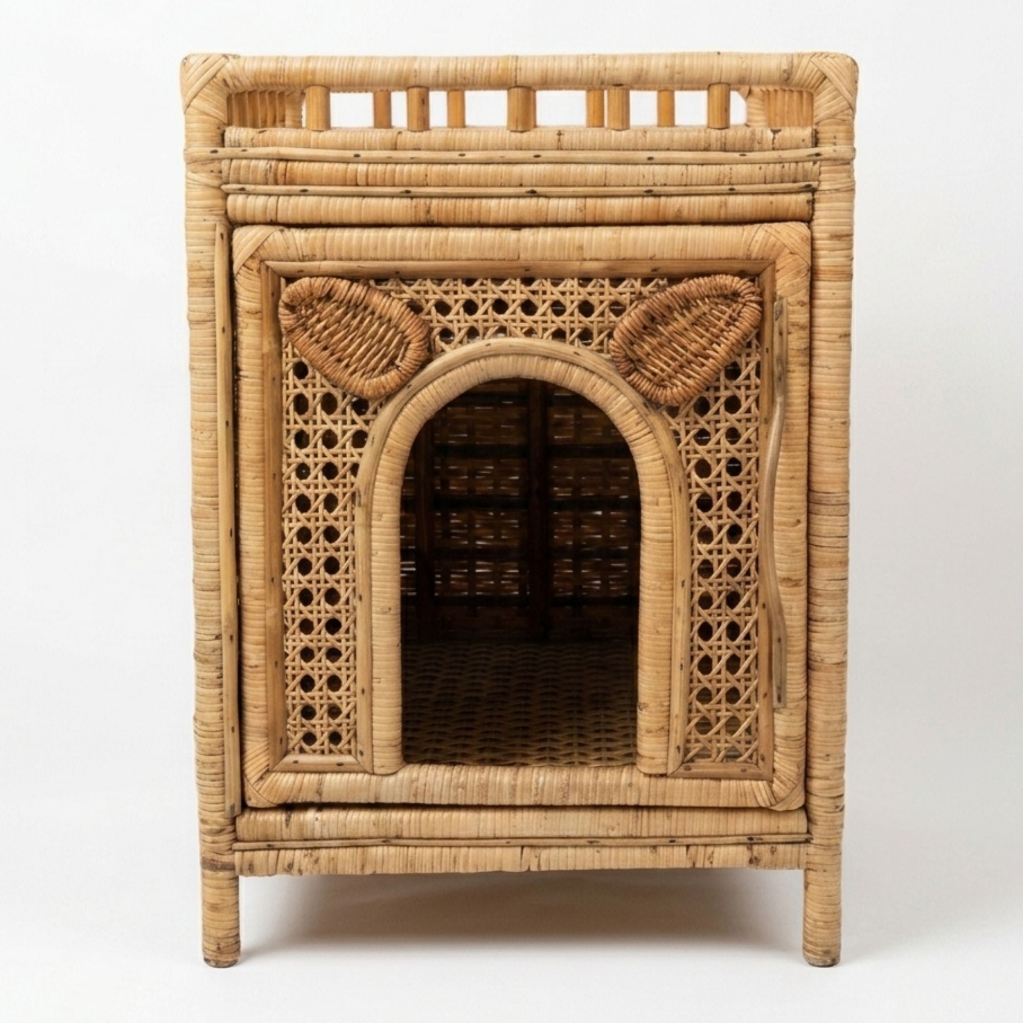 A natural rattan pet house with an arched entryway, woven cane panels, and ear details on the front, shown against a plain white background.